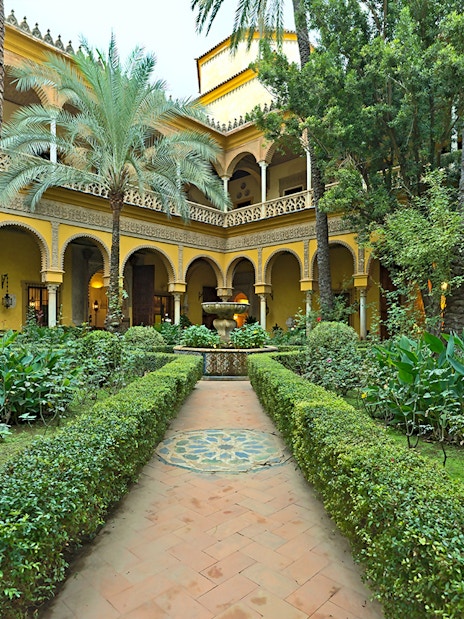 Palacio de las Dueñas courtyard with lush garden and central fountain in Seville.