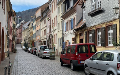Cobblestone street in Heidelberg lined with colorful historic buildings, part of self-guided city exploration game.