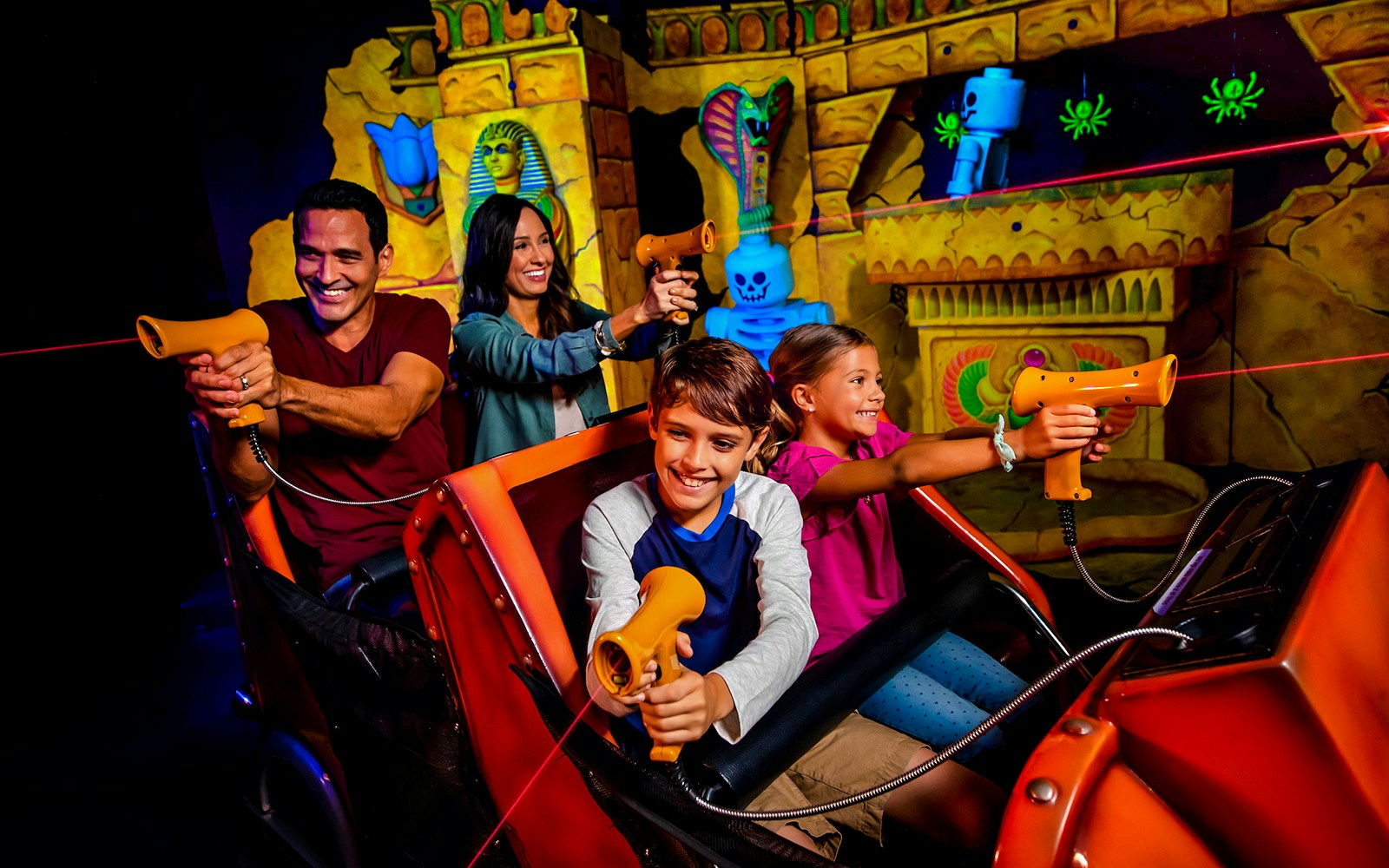 Family enjoying laser ride at Adventure Land, LEGOLAND with colorful Egyptian-themed backdrop.