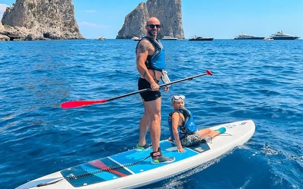 Paddleboarding near Faraglioni rocks in Capri, Italy.
