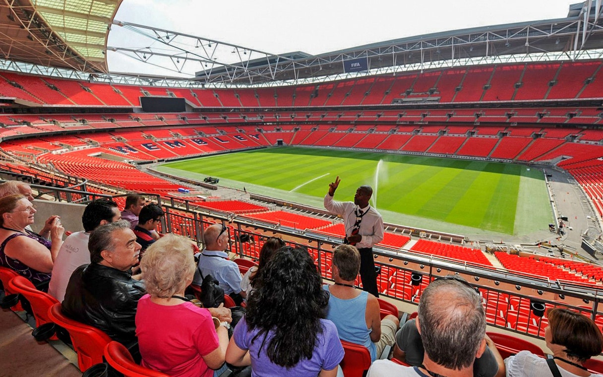 Guide speaking to visitors at Wembley Stadium with view of the field.