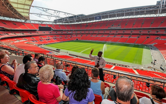 Guide speaking to visitors at Wembley Stadium with view of the field.