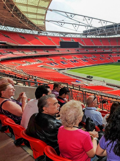 Guide speaking to visitors at Wembley Stadium with view of the field.