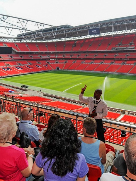 Guide speaking to visitors at Wembley Stadium with view of the field.