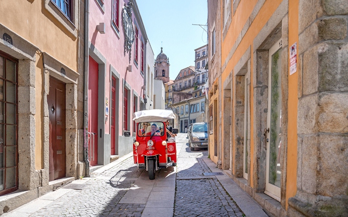 Electric tuk-tuk on a narrow street in Porto, Portugal, with colorful buildings.