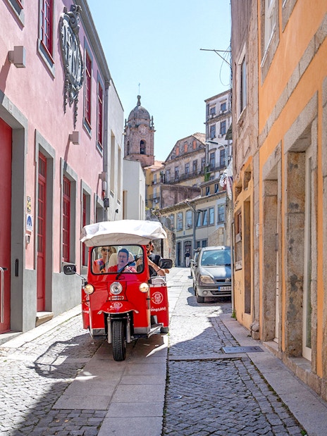 Electric tuk-tuk on a narrow street in Porto, Portugal, with colorful buildings.