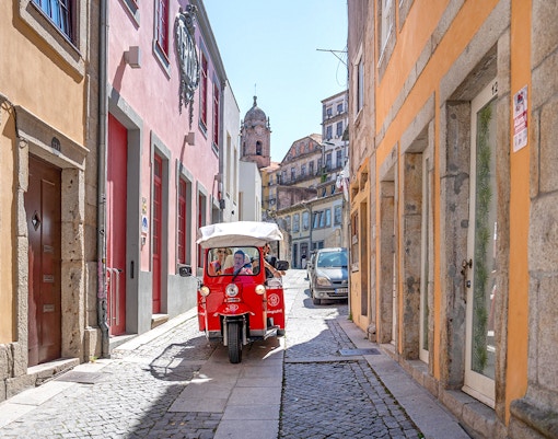 Electric tuk-tuk on a narrow street in Porto, Portugal, with colorful buildings.