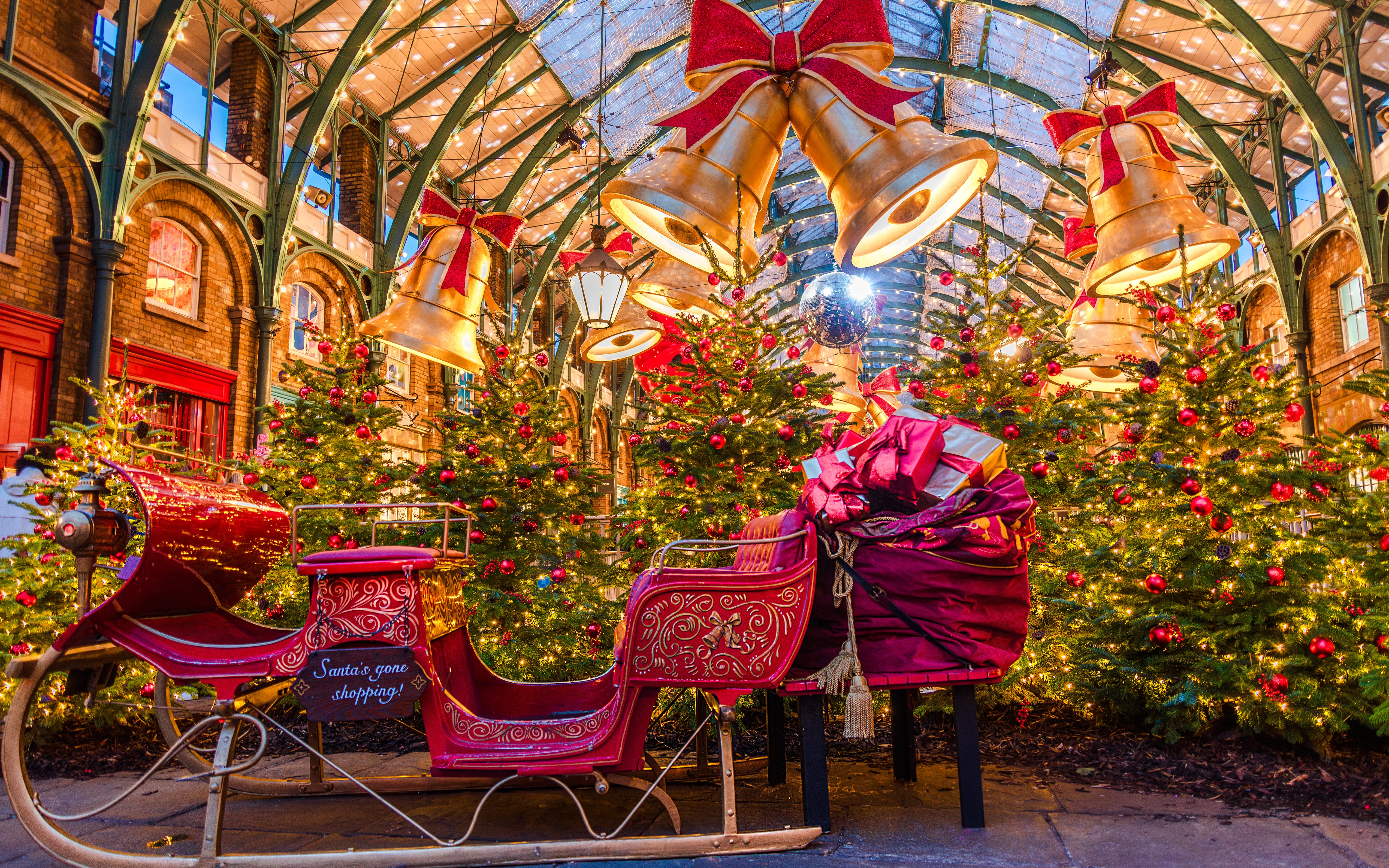 Covent Garden Christmas scene with decorated trees, large bells, and a festive sleigh.