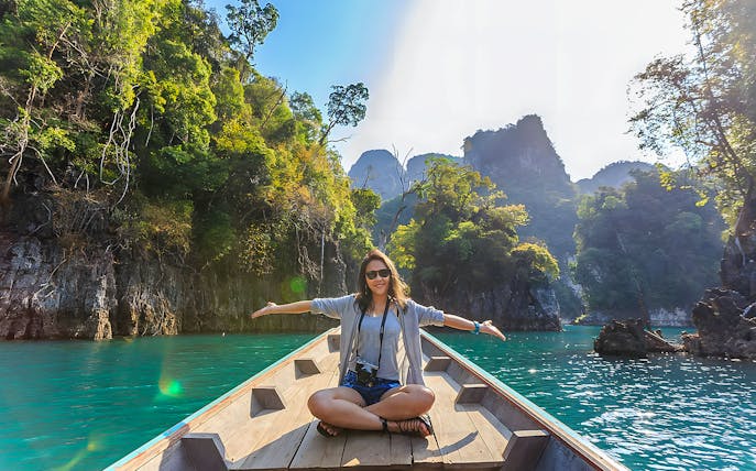 Woman sitting on a long-tail boat in the Andaman Sea with limestone cliffs in the background.