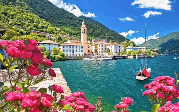 Bellagio village on Lake Como with a boat and vibrant flowers in the foreground.