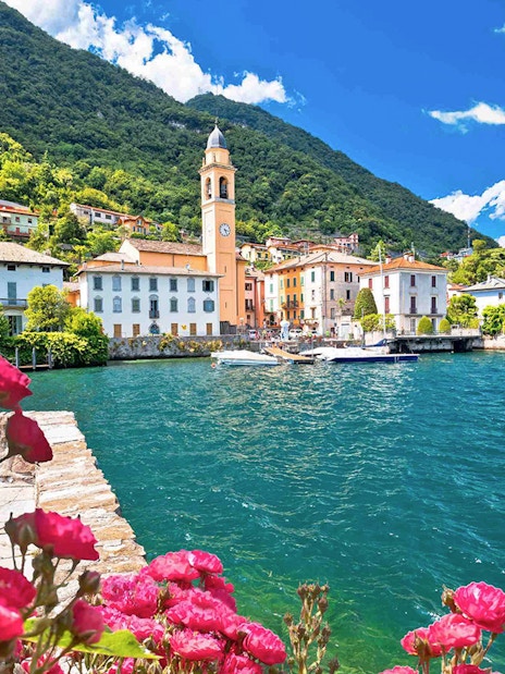 Bellagio village on Lake Como with a boat and vibrant flowers in the foreground.
