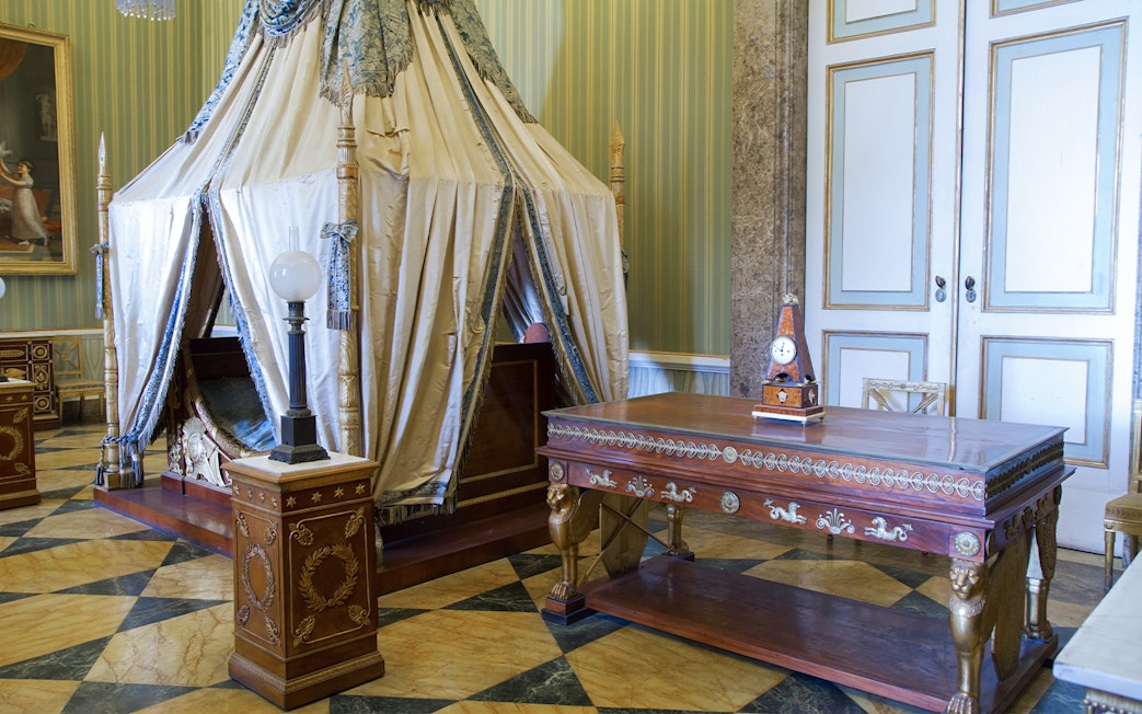 Royal Palace of Caserta interior with ornate canopy bed and decorative wooden table.