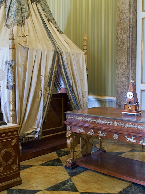 Royal Palace of Caserta interior with ornate canopy bed and decorative wooden table.