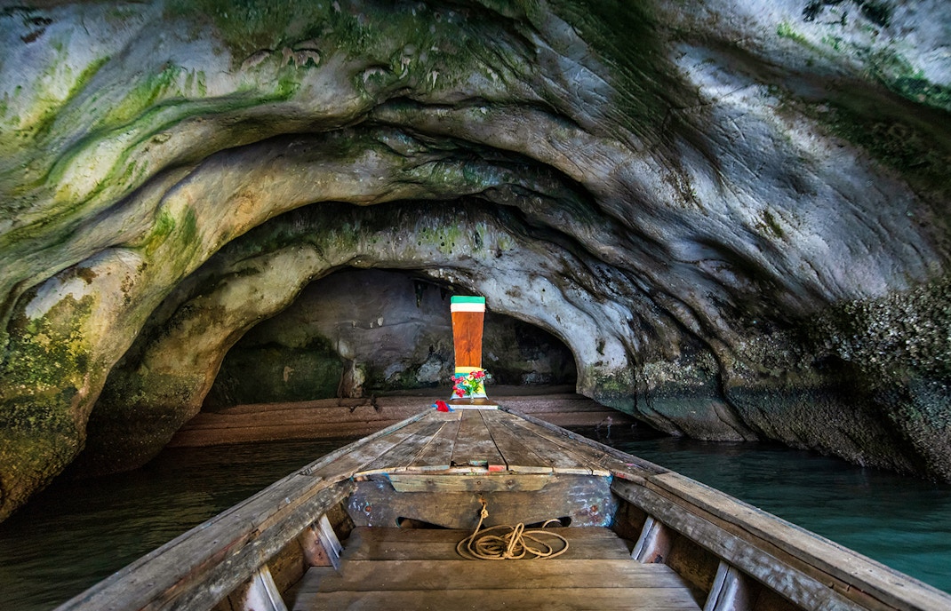 Longtail boat entering Diamond Cave, Thailand, with rocky walls and green moss.