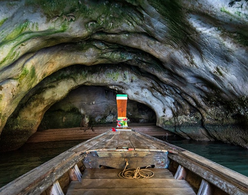 Longtail boat entering Diamond Cave, Thailand, with rocky walls and green moss.