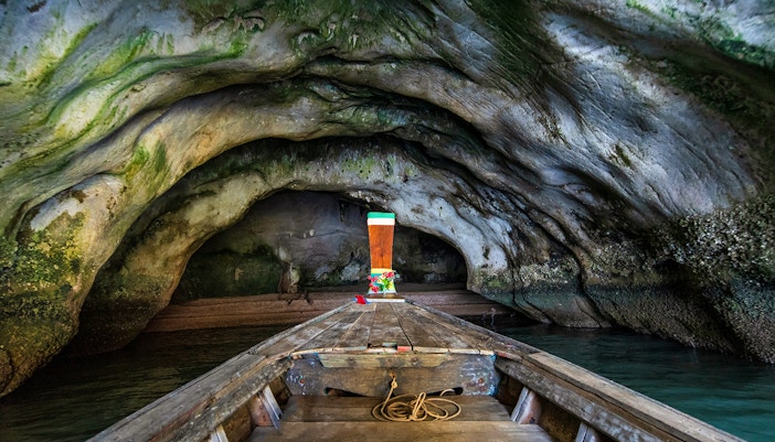 Longtail boat entering Diamond Cave, Thailand, with rocky walls and green moss.