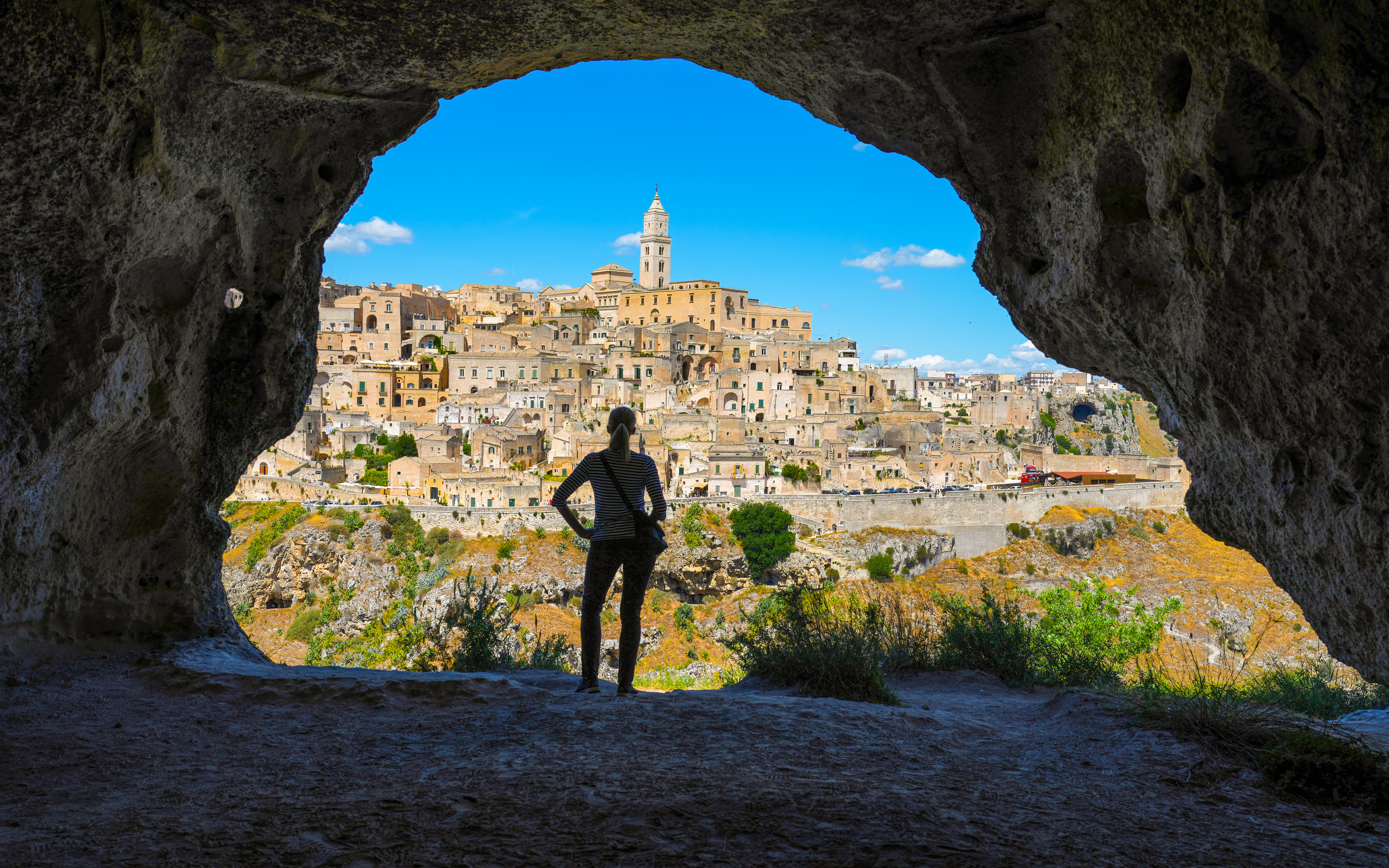 Woman viewing Matera skyline from cave across canyon, Italy.