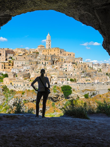 Woman viewing Matera skyline from cave across canyon, Italy.