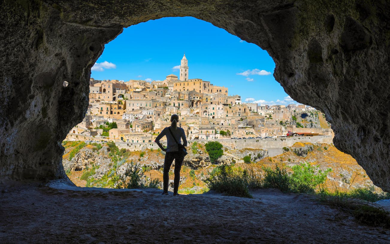 Woman viewing Matera skyline from cave across canyon, Italy.