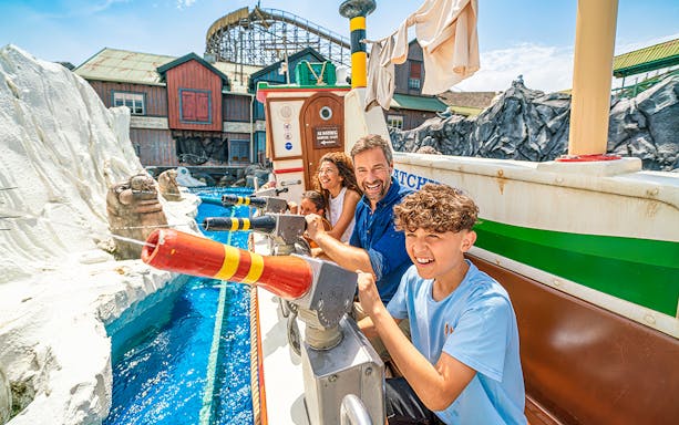Group enjoying a water ride with water cannons on Fjord Rafting, theme park backdrop.