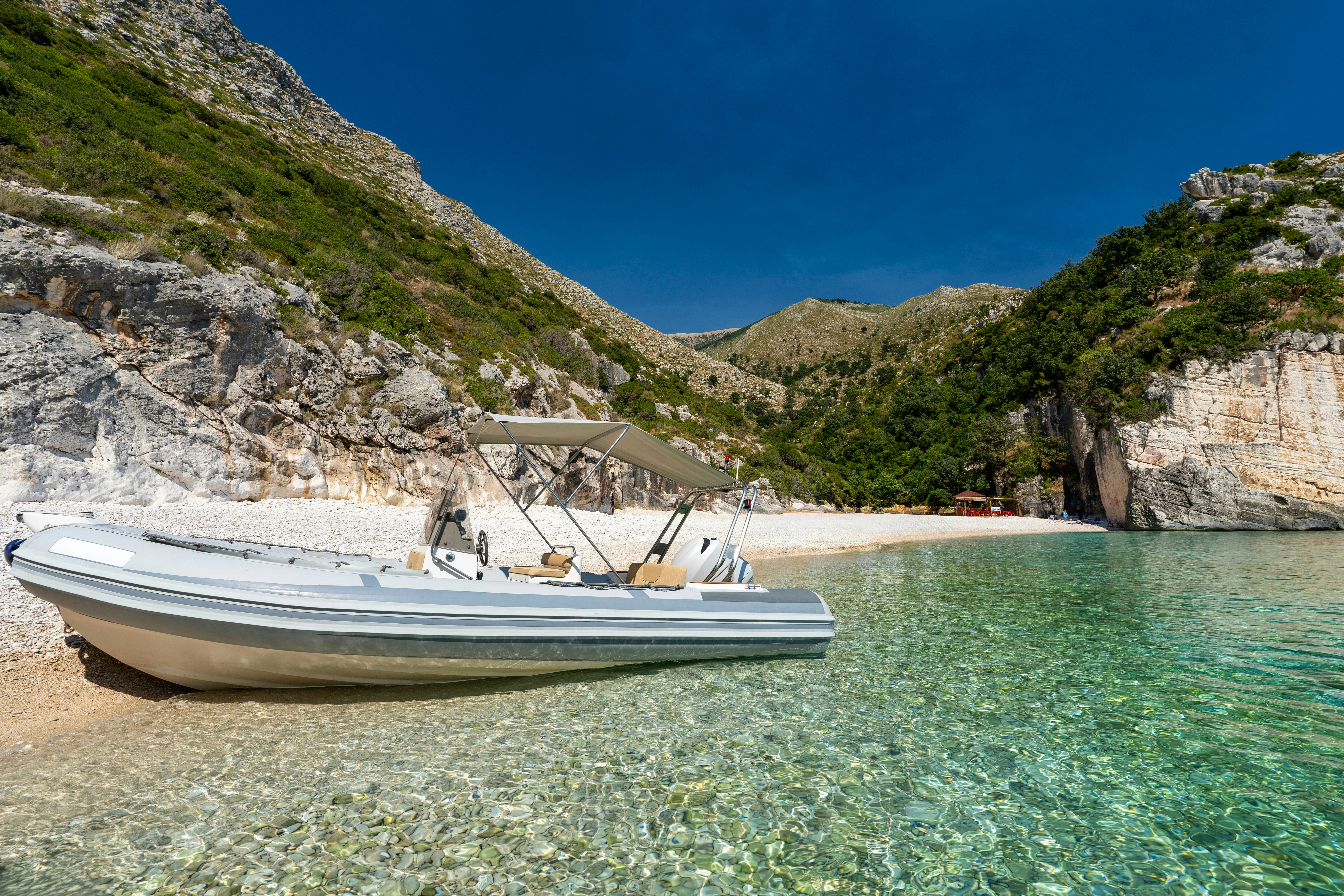 Boat on clear waters at Grama Bay, Albania, with rocky cliffs and a secluded beach.