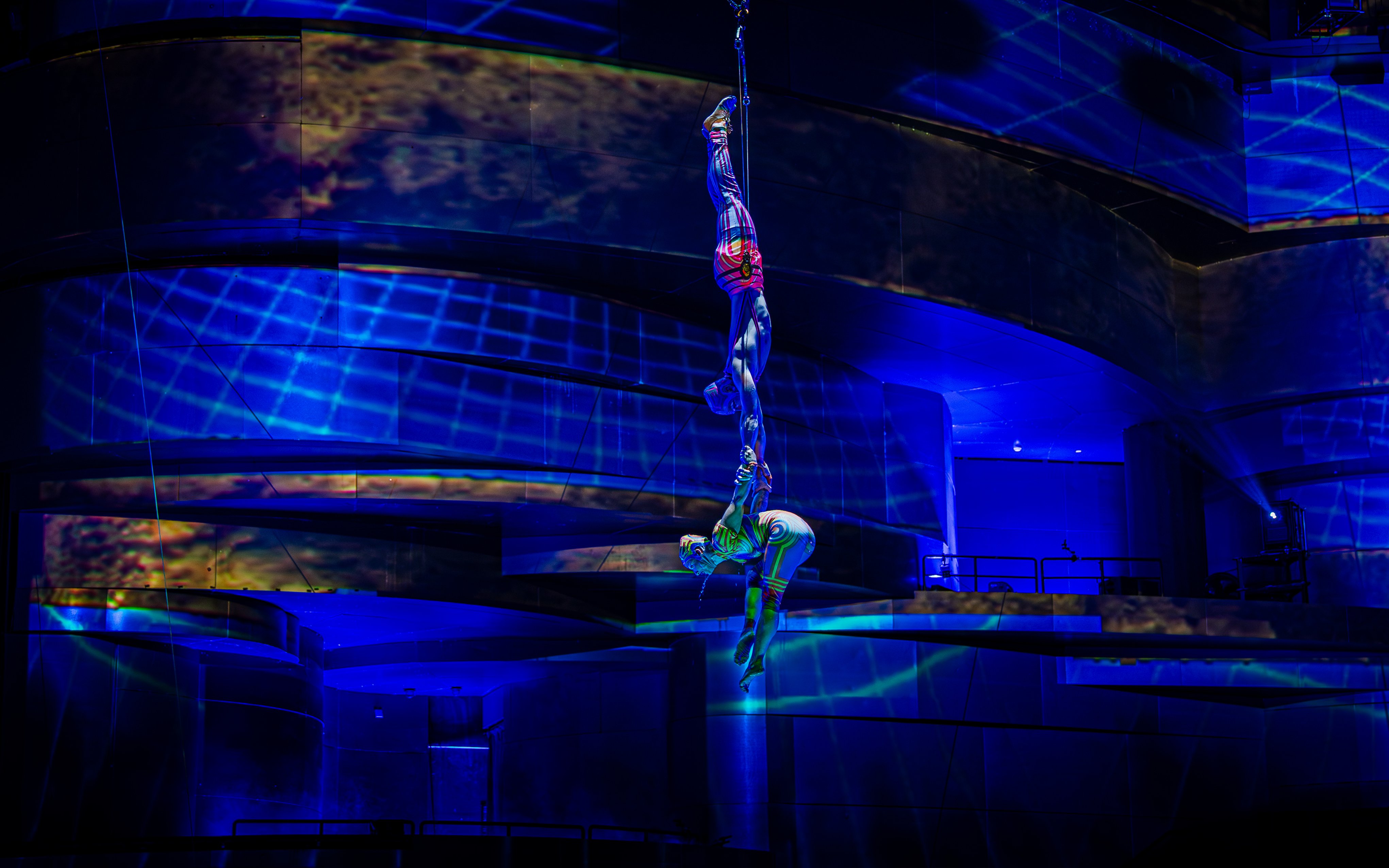 Acrobats performing aerial act at La Perle show in Chapelle, illuminated by blue lights.