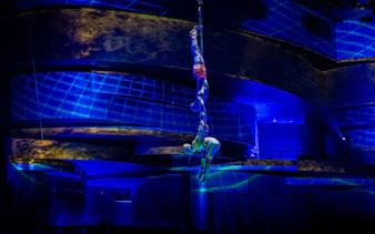 Acrobats performing aerial act at La Perle show in Chapelle, illuminated by blue lights.