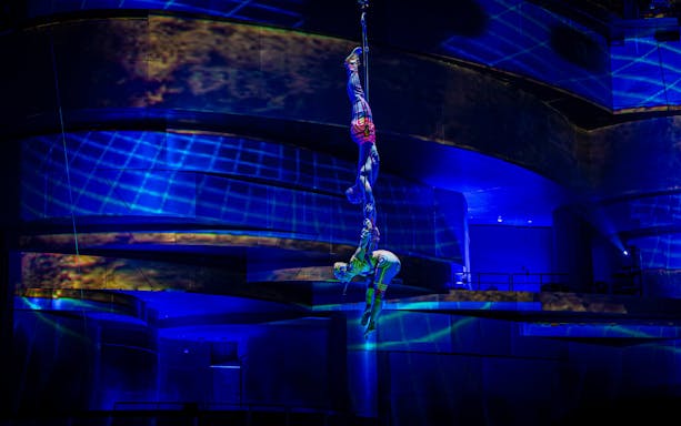 Acrobats performing aerial act at La Perle show in Chapelle, illuminated by blue lights.