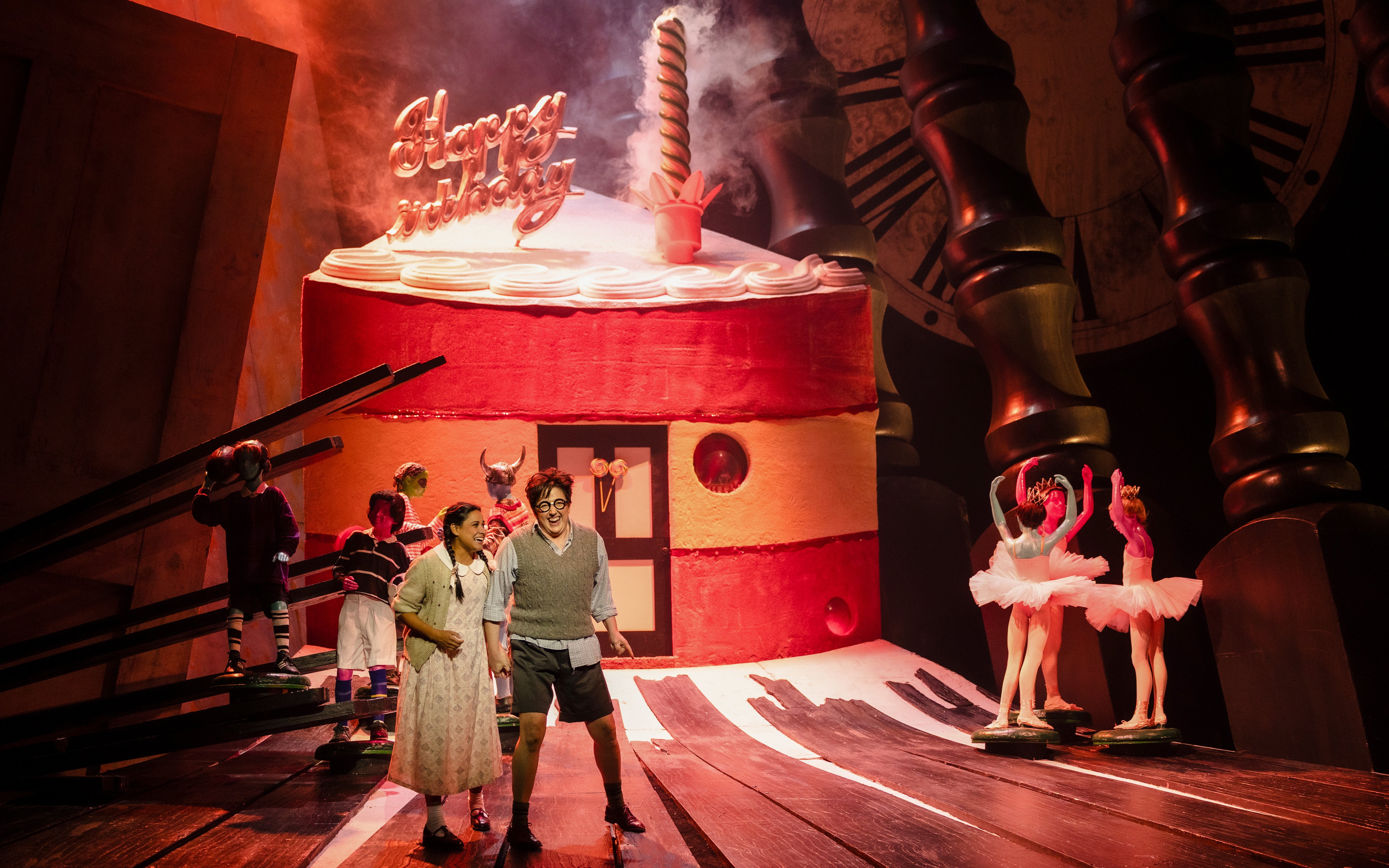 Stage performance of Hansel and Gretel with actors in front of a giant cake set.