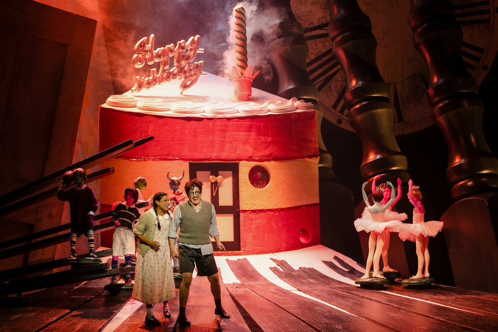 Stage performance of Hansel and Gretel with actors in front of a giant cake set.