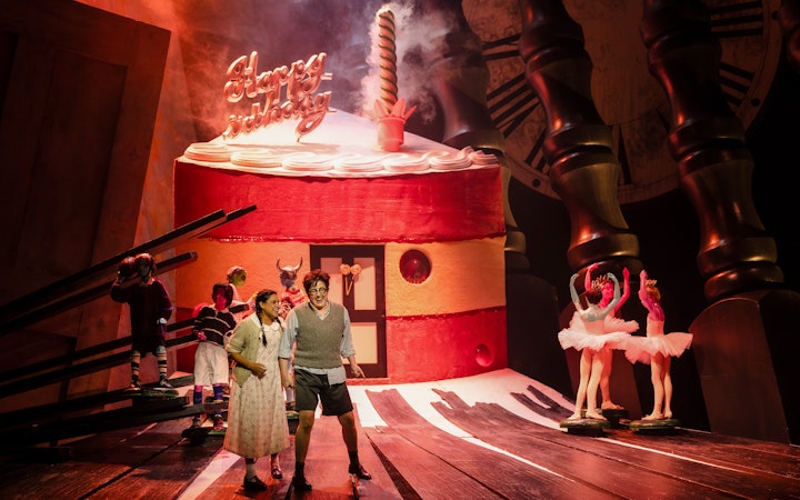 Stage performance of Hansel and Gretel with actors in front of a giant cake set.