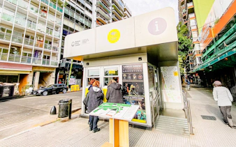 Tourists at Buenos Aires information center kiosk with city map and tango show poster.