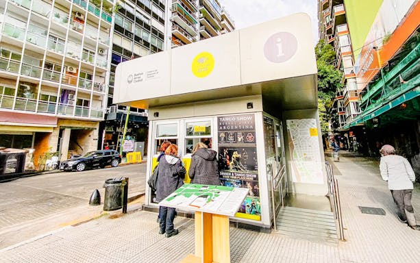 Tourists at Buenos Aires information center kiosk with city map and tango show poster.