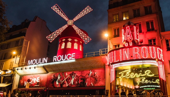Moulin Rouge Paris exterior illuminated at night with vibrant lights and iconic windmill.