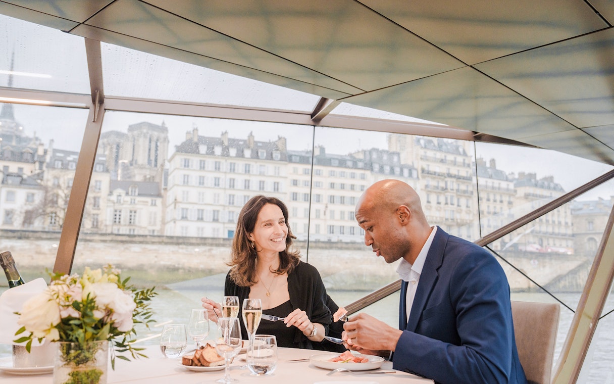 Couple dining on a Seine River sightseeing lunch cruise with Parisian architecture in the background.