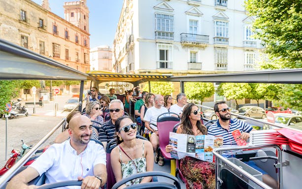 Tourists enjoying a Hop-On Hop-Off bus ride in Cadiz, passing historic buildings.