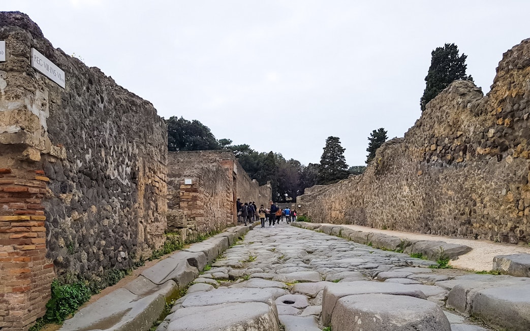 Tourists walking along ancient stone street in Pompeii, Italy.