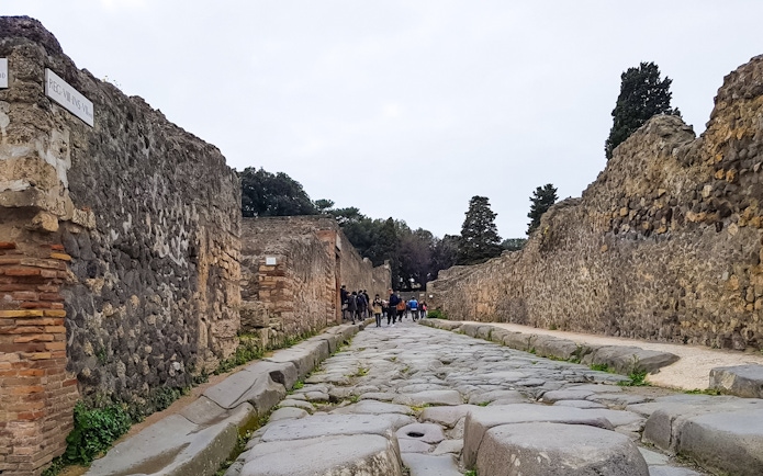 Tourists walking along ancient stone street in Pompeii, Italy.