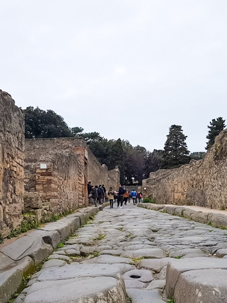 Tourists walking along ancient stone street in Pompeii, Italy.