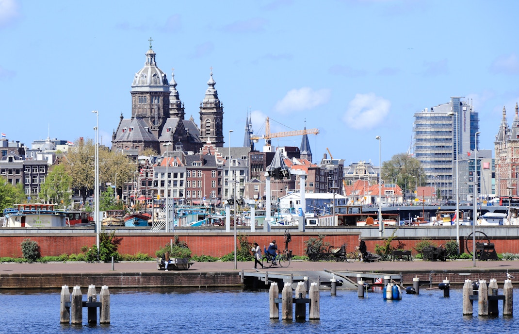 Amsterdam Oosterdok view with people, boats, and St. Nicholas Basilica in the background.