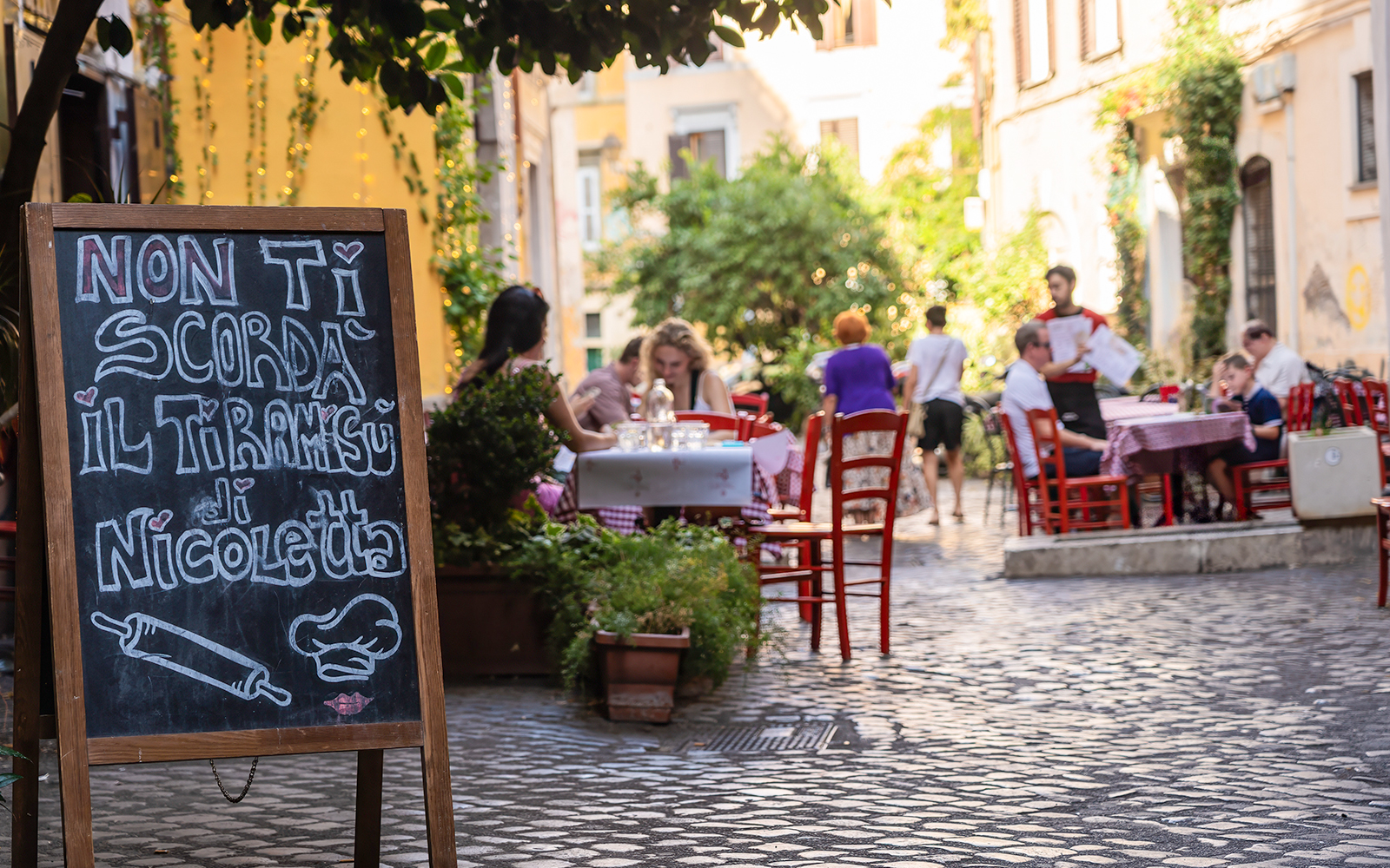 Cobblestone street cafe in Rome with outdoor seating and menu board.