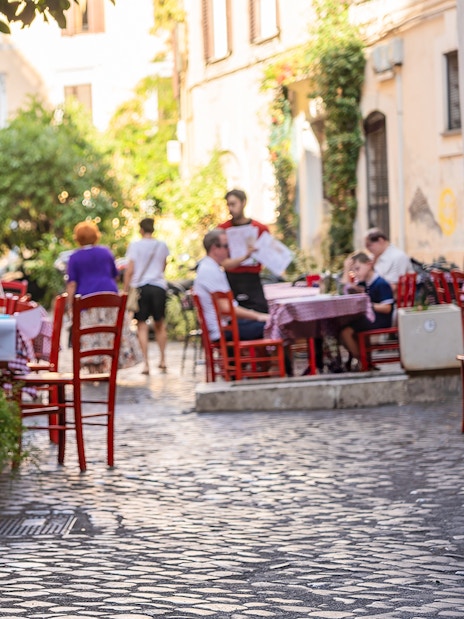 Cobblestone street cafe in Rome with outdoor seating and menu board.