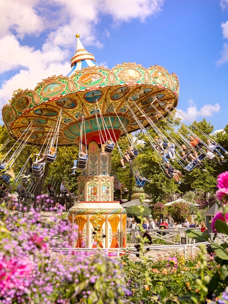 Carousel swing ride at Tivoli Gardens, Copenhagen surrounded by colorful flowers.