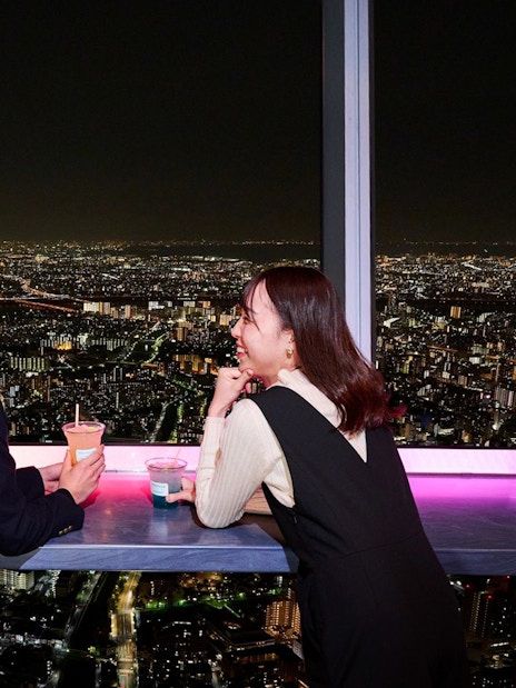 Tourists enjoying drinks with a night view of Tokyo from the Tembo Deck.