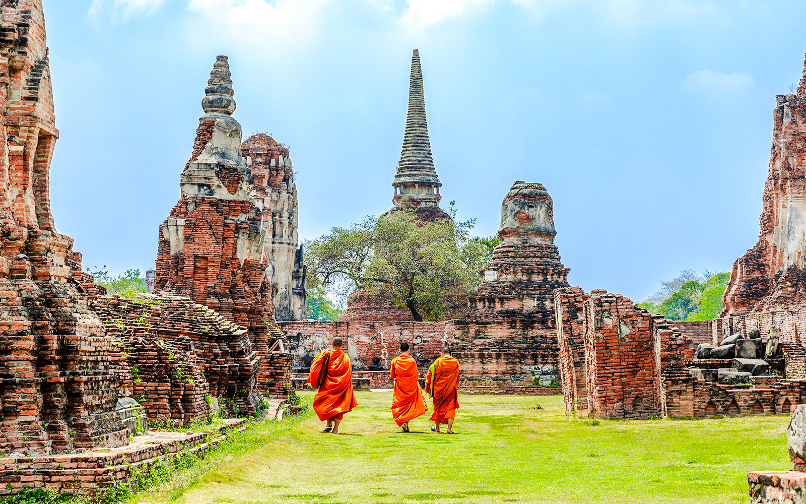 Monks walking through Ayutthaya Historical Park with ancient ruins in the background.