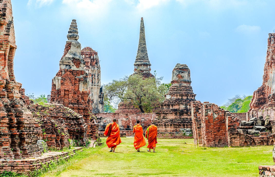Monks walking through Ayutthaya Historical Park with ancient ruins in the background.