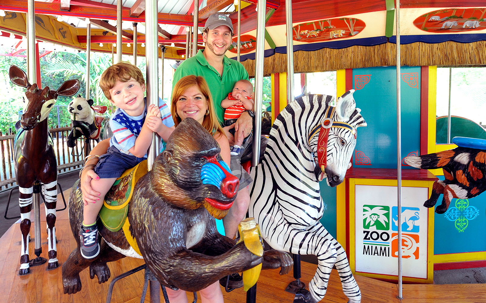Family enjoying carousel ride at Zoo Miami with animal figures.