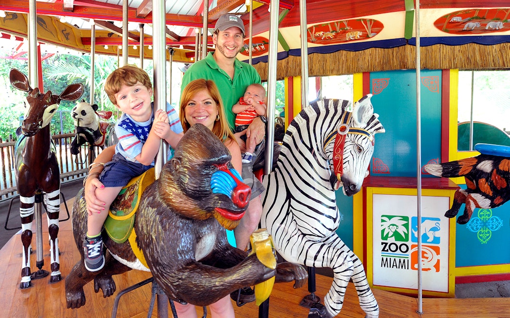 Family enjoying carousel ride at Zoo Miami with animal figures.
