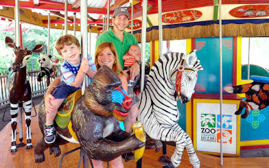 Family enjoying carousel ride at Zoo Miami with animal figures.