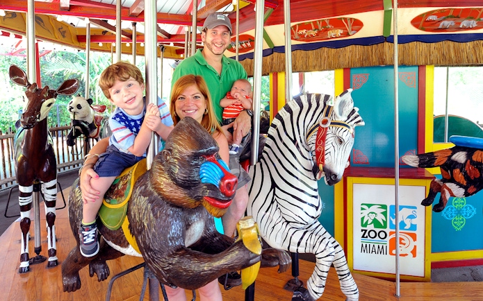 Family enjoying carousel ride at Zoo Miami with animal figures.